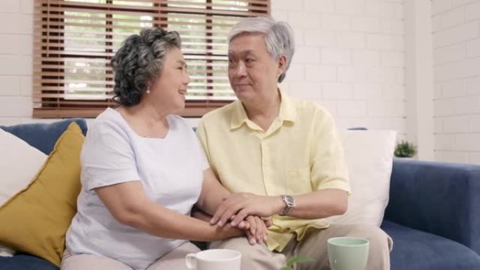 亚洲老年夫妇在客厅里牵着手，夫妻在家里躺在沙发上感到幸福的分享和支持。生活方式高级家庭在家的概念。