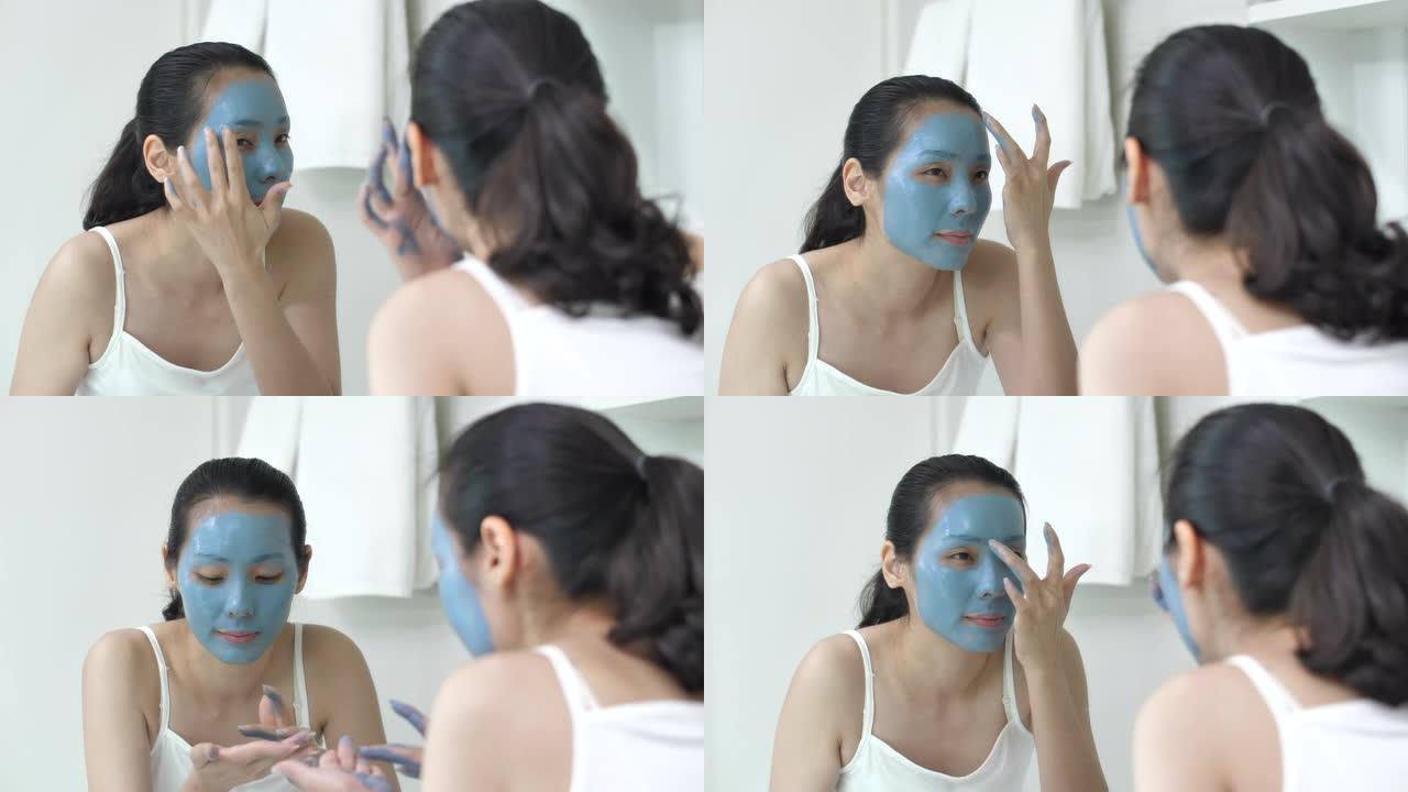 亚洲人在家里的浴室里给她脸上戴上蓝色保湿面膜