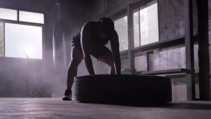 剪影强壮的男人在推轮胎。男人用大轮胎锻炼。在健身房刻苦训练。武术
