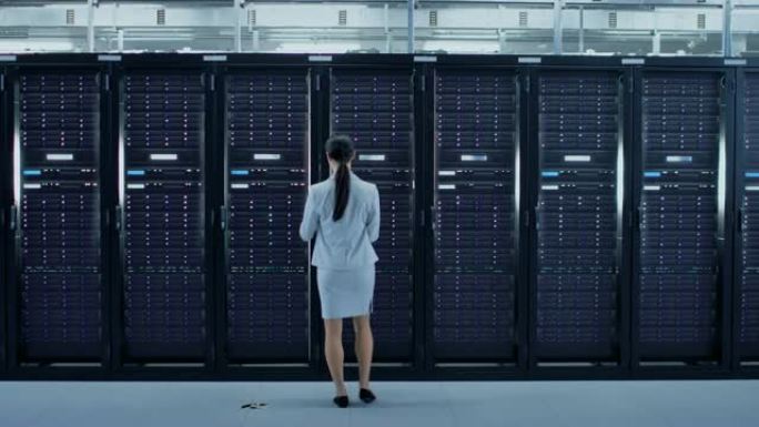 女性数据中心it技术人员带着笔记本电脑走过服务器机架走廊。她正在目视检查工作服务器机柜。