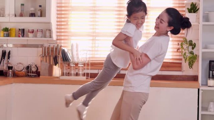 亚洲家庭的母亲和可爱的小孩女儿一起在厨房跳舞，快乐的家庭母亲和小女孩一起玩得开心，一起在家里玩有趣的