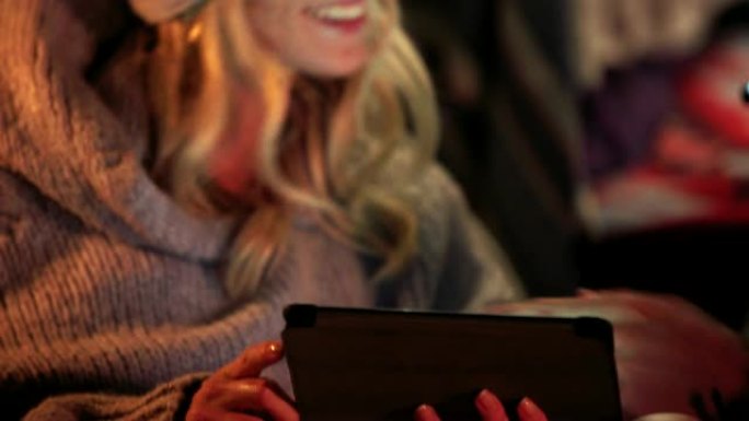 微笑的女人在晚上向朋友展示平板电脑