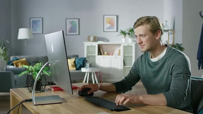 专注的年轻人坐在办公桌前在个人电脑上工作的肖像。背景舒适的客厅。