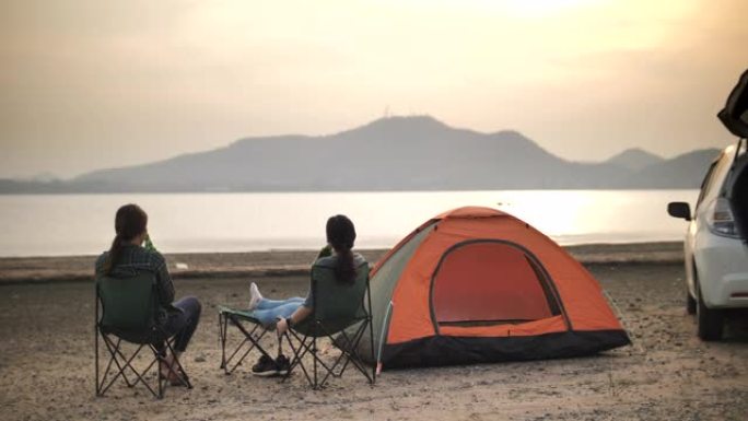 两个亚洲女性朋友在湖附近的露营度假中一起碰杯啤酒瓶