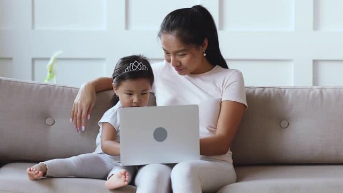 快乐的亚洲女儿学习笔记本电脑和妈妈一起看在线动画片