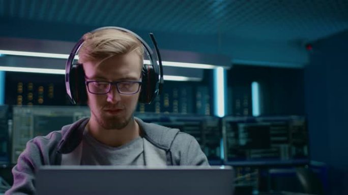 软件开发人员/黑客/游戏玩家的肖像，戴着眼镜和耳机坐在办公桌前，在笔记本电脑上工作/玩。在背景中，具