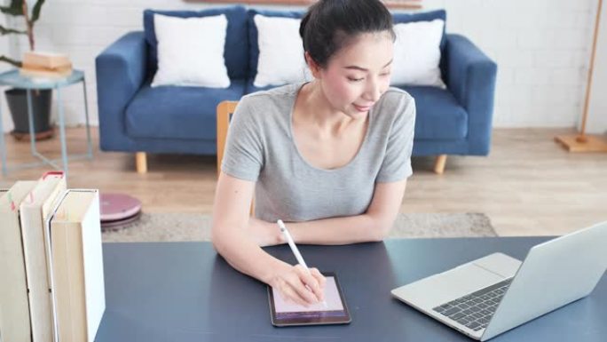 亚洲年轻女子使用数字平板电脑在家在线学习。新的家庭办公室设置