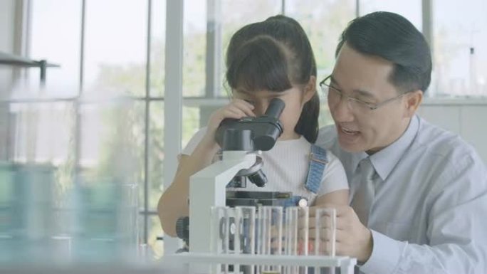 亚洲男科学家在教室实验室用显微镜教小女孩科学实验。有科教理念的人。
