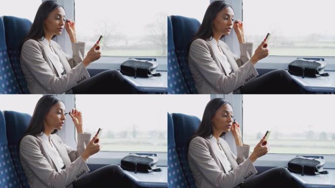 女商人坐在火车上通勤上班，用手机当镜子化妆