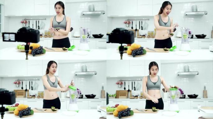 年轻的亚洲女性有影响力的vlogger穿着运动服，在厨房里制作果汁或水果。