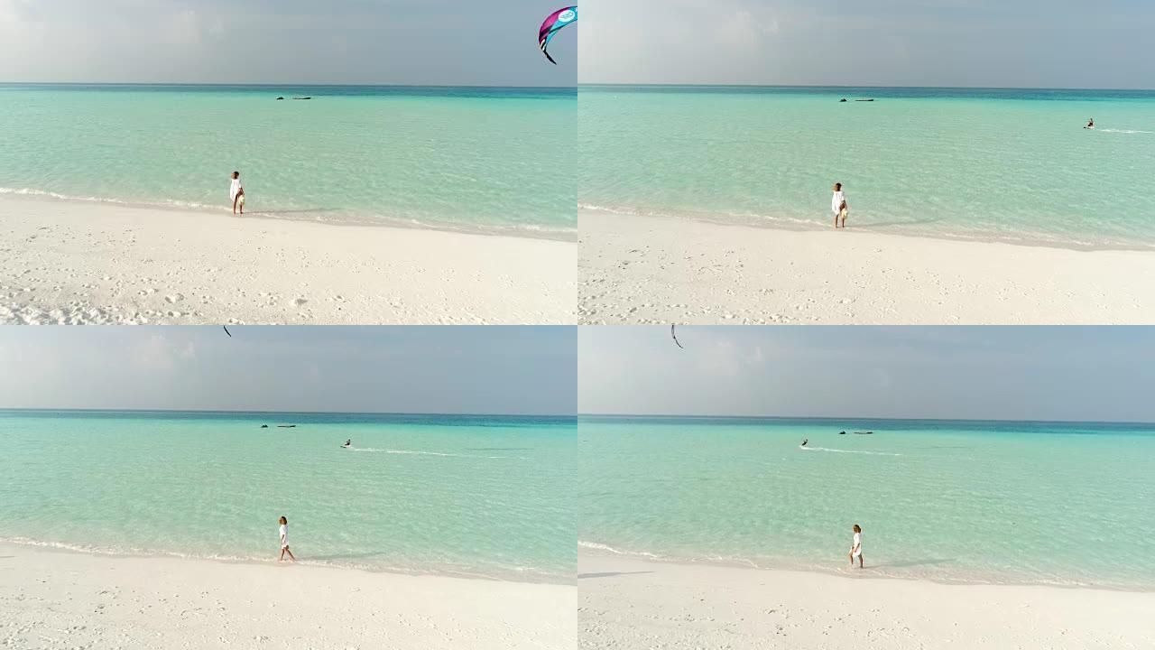 WS女人在阳光明媚的热带海滩上行走，看着风筝冲浪者马尔代夫