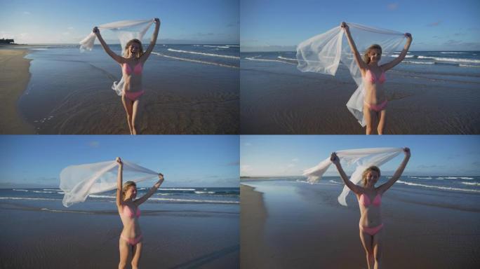 南非，一个微笑的美丽年轻女子站在海滩浅水中，拿着白色纱笼，4k慢动作视图