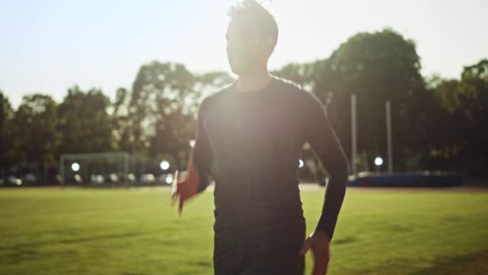 穿着灰色衬衫和短裤的运动健美男子在体育场慢跑。在一个温暖的夏日下午，他跑得很快。运动员做他的常规运动