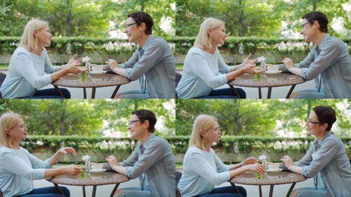 成熟的女士在露天咖啡馆和朋友聊天，在桌子上笑得很开心