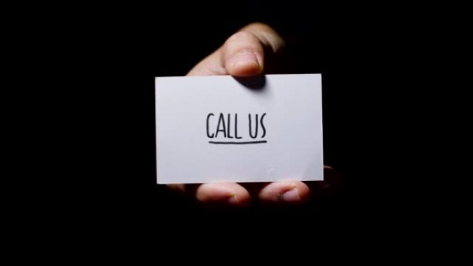 一只手显示一张卡片，上面写着: “打电话给我们”，孤立在黑色背景上。