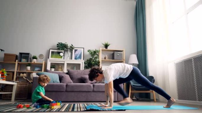 现代家庭主妇在做瑜伽，而她的小孩在地毯上玩积木