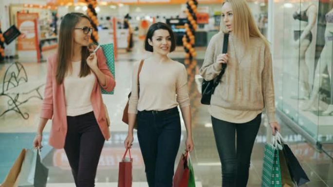 漂亮的年轻女性在购物中心里背着纸袋购物时聊天。零售、快乐顾客和青年生活理念。