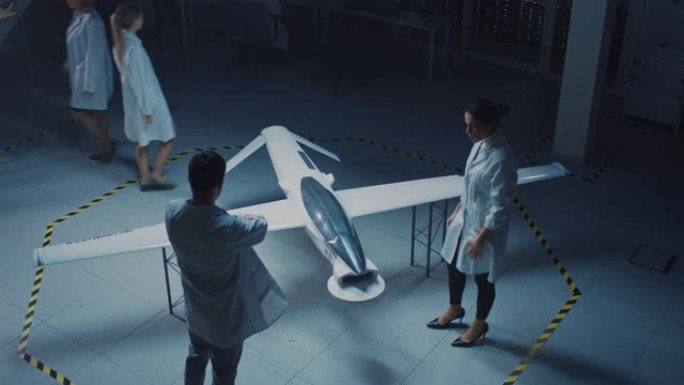 两名航空航天工程师在无人飞行器/无人机原型上工作。航空专家穿着白大褂说话，使用平板电脑。带有监视或军