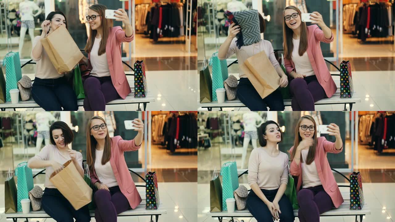 现代年轻女性正在使用智能手机从购物中心拨打在线视频电话。女孩们在聊天和笑，展示购买的衣服和挥舞的手。