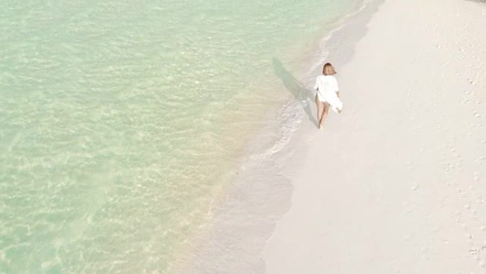 女士在马尔代夫阳光明媚的田园诗般的热带海滩上行走