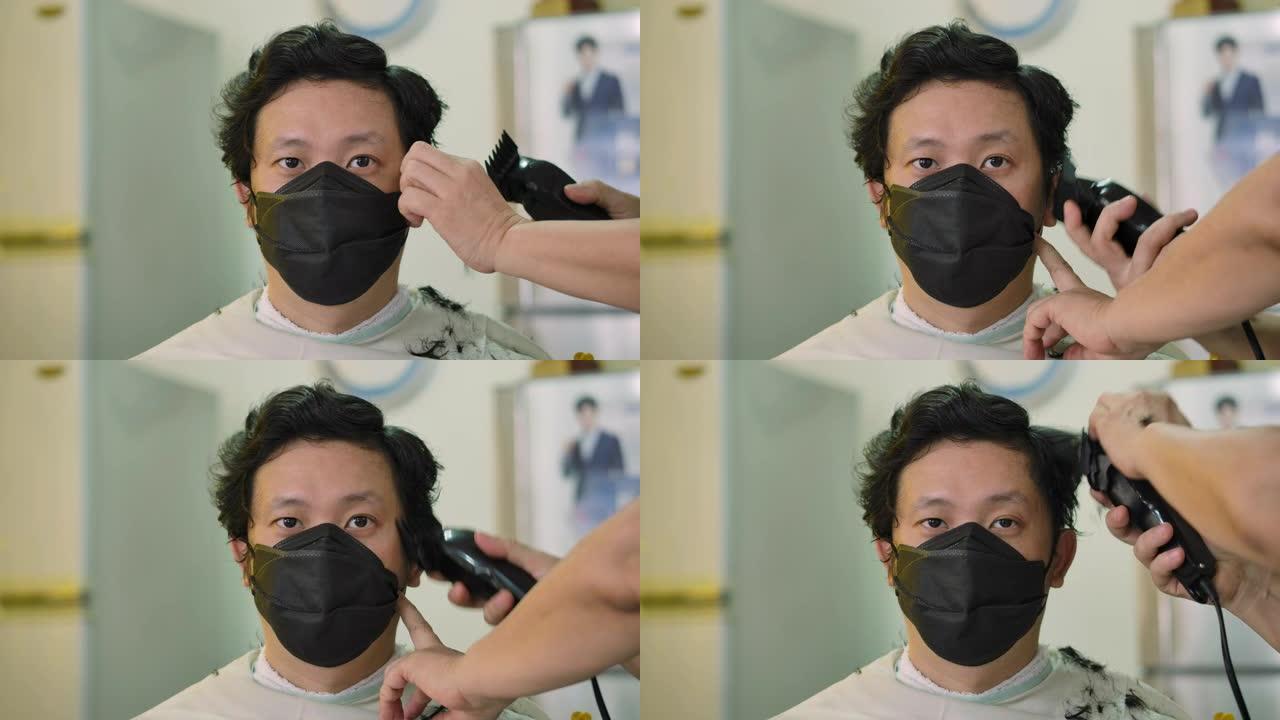 一名年轻帅气的男子戴着医用防护口罩，在隔离期间在家理发时看着镜头。居家隔离冠状病毒大流行预防，社会隔