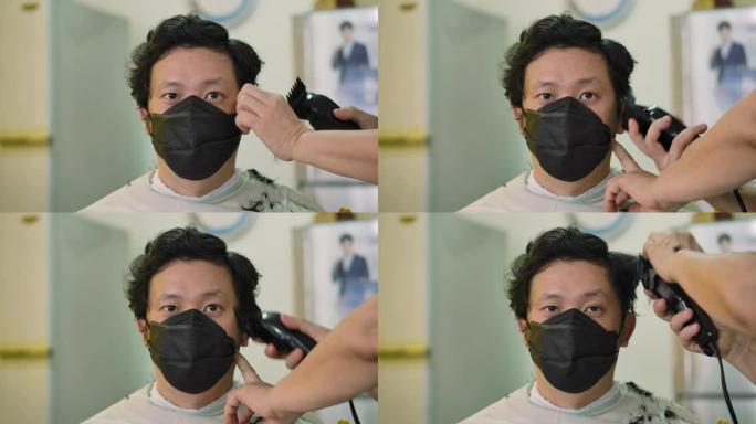 一名年轻帅气的男子戴着医用防护口罩，在隔离期间在家理发时看着镜头。居家隔离冠状病毒大流行预防，社会隔
