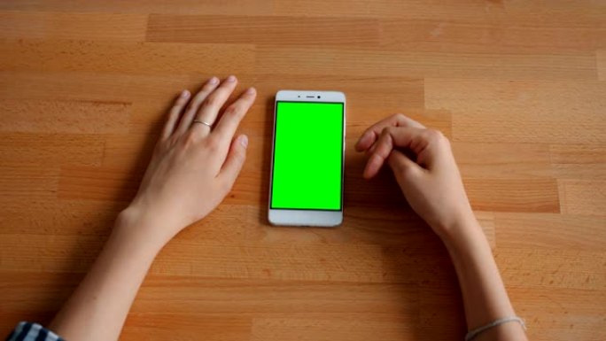 女性手触摸绿色模型智能手机屏幕躺在木桌上