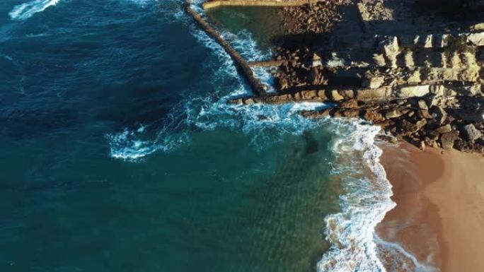 自上而下的空中无人机镜头: 葡萄牙岩石海岸，美丽的海景。抽象自然，海岸线上碧绿的海浪在沙滩上滚动。P