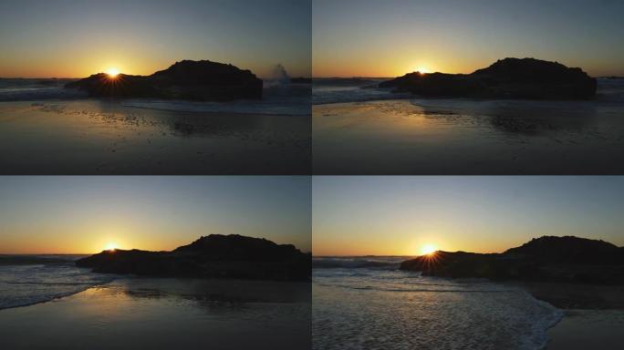 海滩上湿沙的景色和大西洋海浪淹没了它。太阳在葡萄牙日落时滑动一块黑色的岩石。UHD