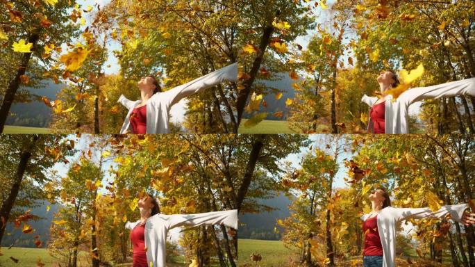 特写: 快乐的女孩伸出双臂，五颜六色的树叶从树梢上掉下来