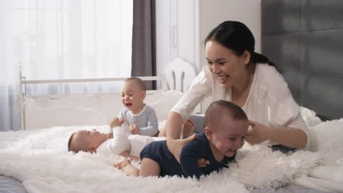 充满爱心的亚洲妈妈和1岁的三胞胎坐在床上