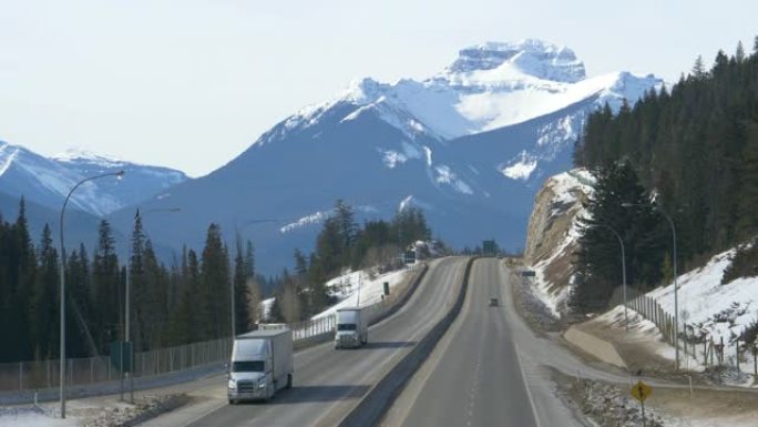 无人机: 在阳光明媚的冬日，两辆货运卡车沿着加拿大横贯公路行驶。