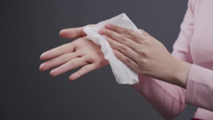 亚洲妇女用婴儿擦纸清洁她的脏手。成年妇女用白色湿纸巾清理她的手。带有复制空间的灰色背景上的医疗保健，