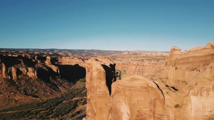 无人机飞越巨大的岩石，揭示了阳光明媚的岩石沙漠中峡谷山脊之间的宏伟公路。