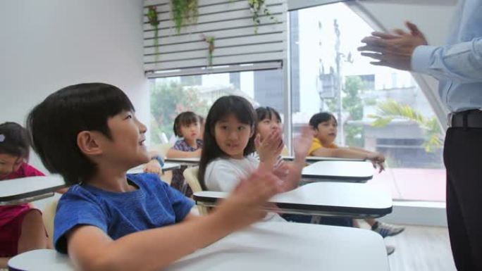 一群学校的孩子，老师坐在教室里举手。小学，人民，学习，教育和学校概念。技术和儿童概念。