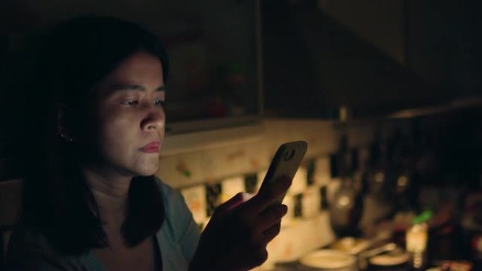 年轻的亚洲女性手持设备在公寓发送电子邮件。