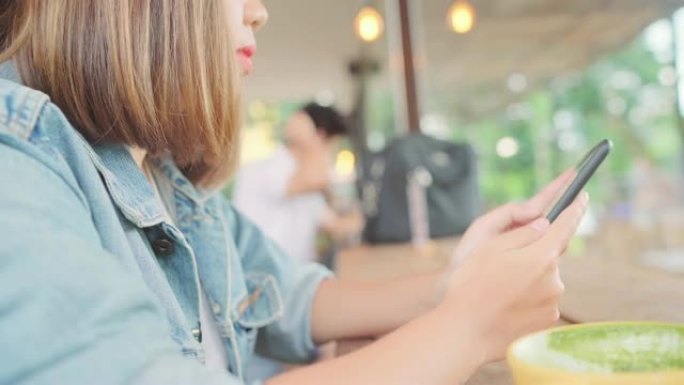 商业自由亚洲女性坐在咖啡馆的桌子上时，使用智能手机聊天，阅读和发短信。生活方式聪明的美女在咖啡店工作