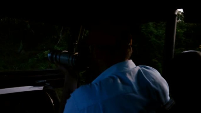 年轻快乐好奇的摄影师男子在野生动物园游览汽车之旅中，用专业相机在森林之旅中拍照。