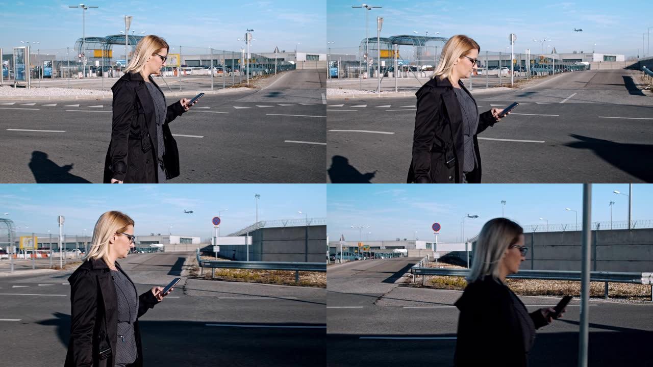 带着智能手机走在机场人行道上的女商人女士，飞机正在降落。