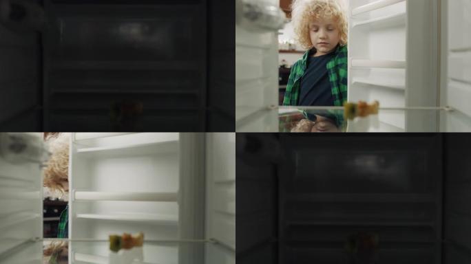 饥饿的男孩在家里的空冰箱里寻找食物