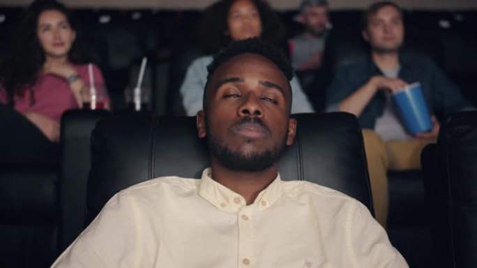昏昏欲睡的非洲裔美国学生在电影院看电影闭眼眨眼