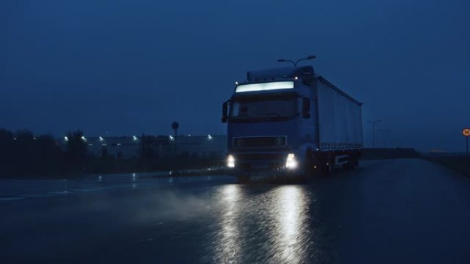 满载货物拖车的长途半卡车在夜间在高速公路上行驶，穿过雨、雾、雪穿越大陆。工业仓库区。慢动作拍摄后的正