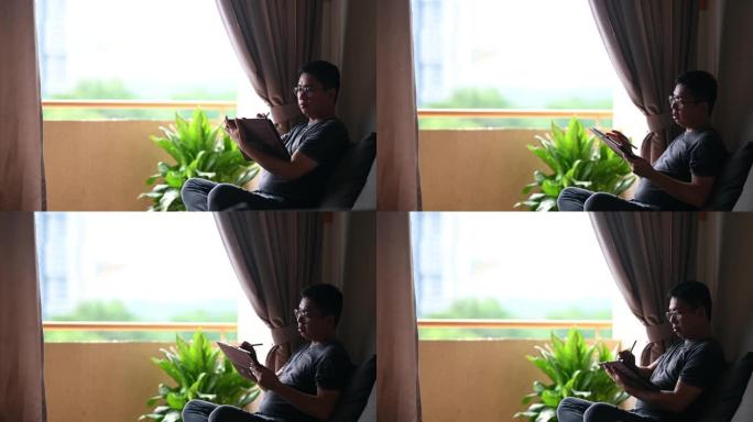 一名亚洲中国中年男子在家中使用数字平板电脑进行drraw