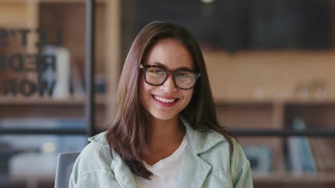千禧一代亚洲女性创意戴眼镜，坐在办公室对着镜头微笑，特写镜头