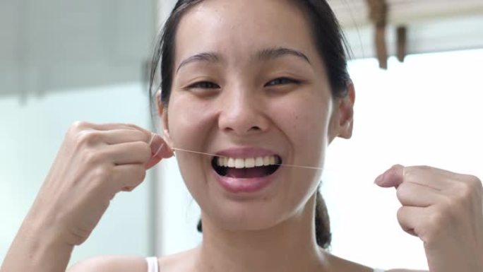 年轻的亚洲妇女用牙线在家里的浴室里看着相机