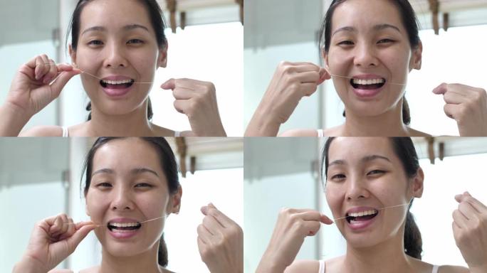 年轻的亚洲妇女用牙线在家里的浴室里看着相机