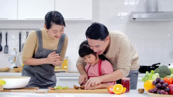幸福的年轻家庭，妈妈，爸爸和年轻女孩在厨房做饭，一起做饭