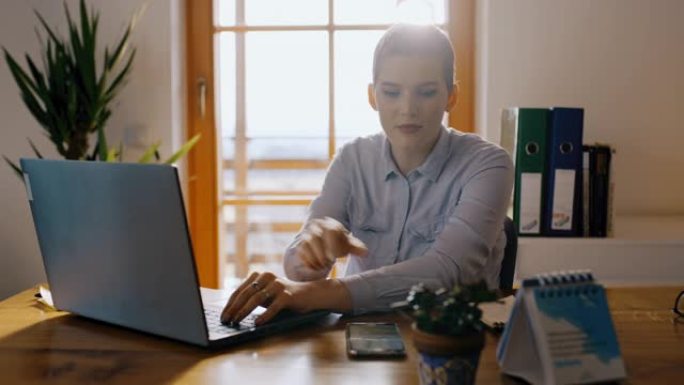 DS女人在家里用笔记本电脑工作时检查手机