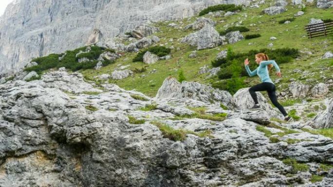 年轻的健康的运动女人跑出了一条被人走过的小路，爬上陡峭的岩石山