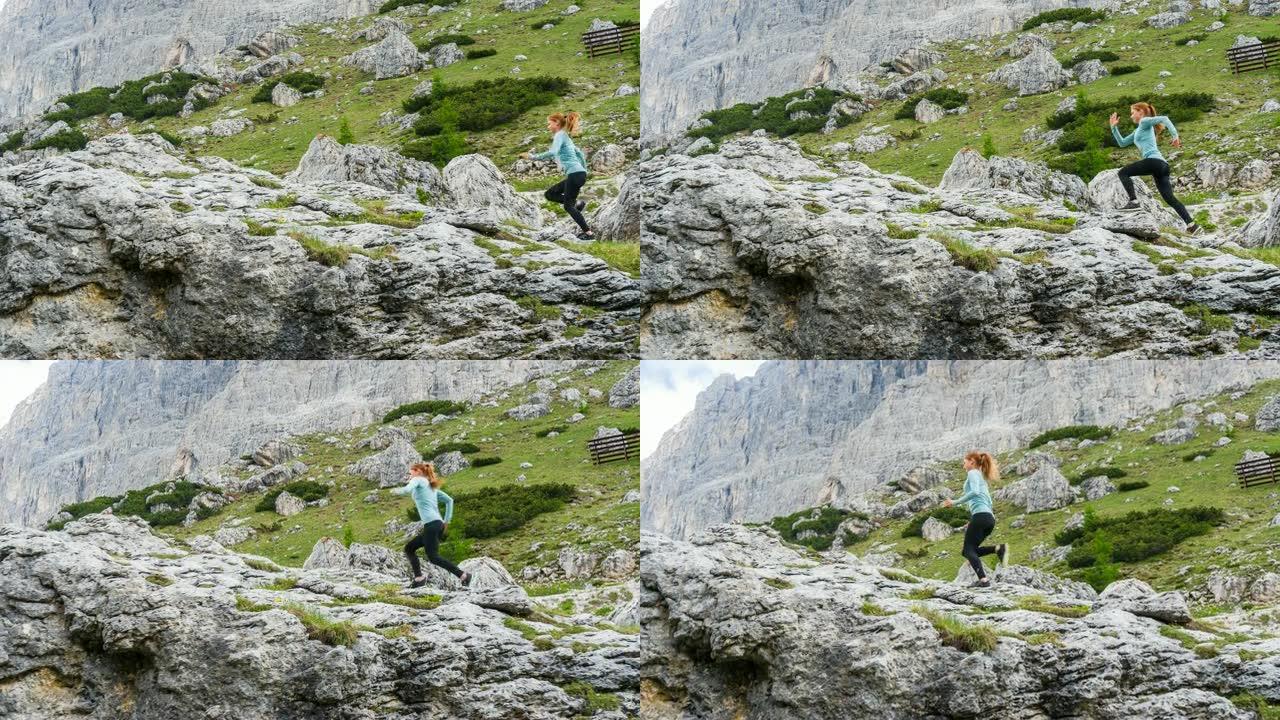年轻的健康的运动女人跑出了一条被人走过的小路，爬上陡峭的岩石山